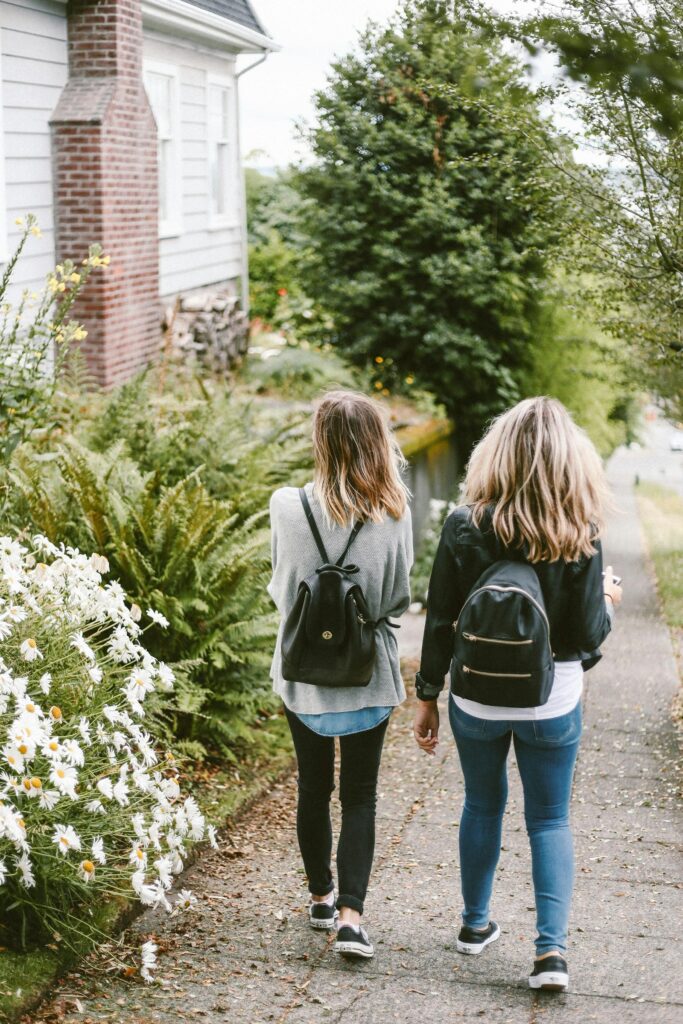 Two people walking together along a leafy path, seen from behind.